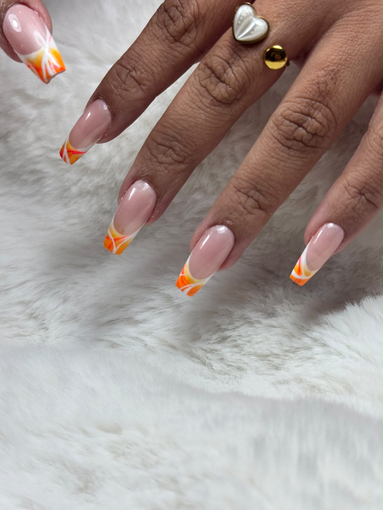 French orange et jaune sur base nude, main posée sur une fourrure blanche avec bague cœur