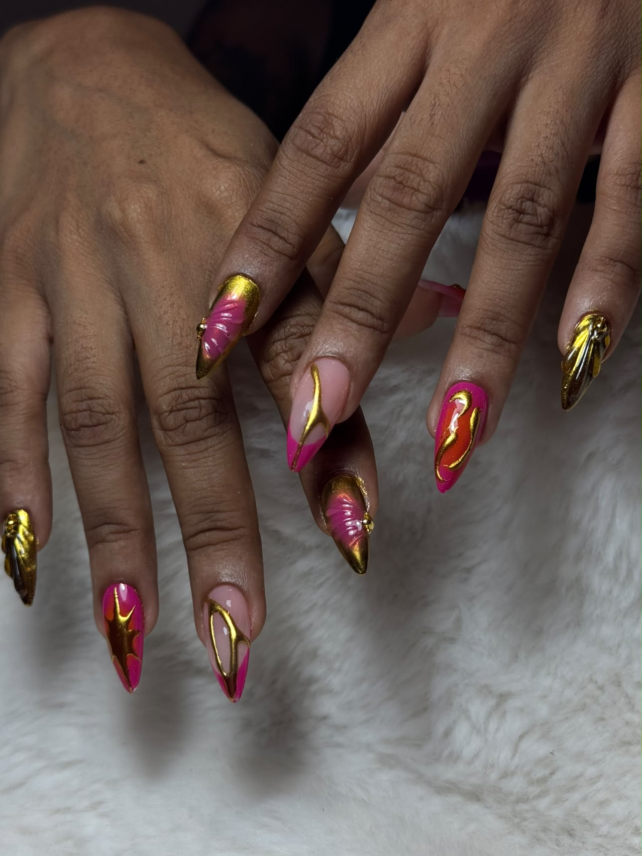 Deux mains aux ongles stiletto roses et nude, ornés de motifs dorés en relief