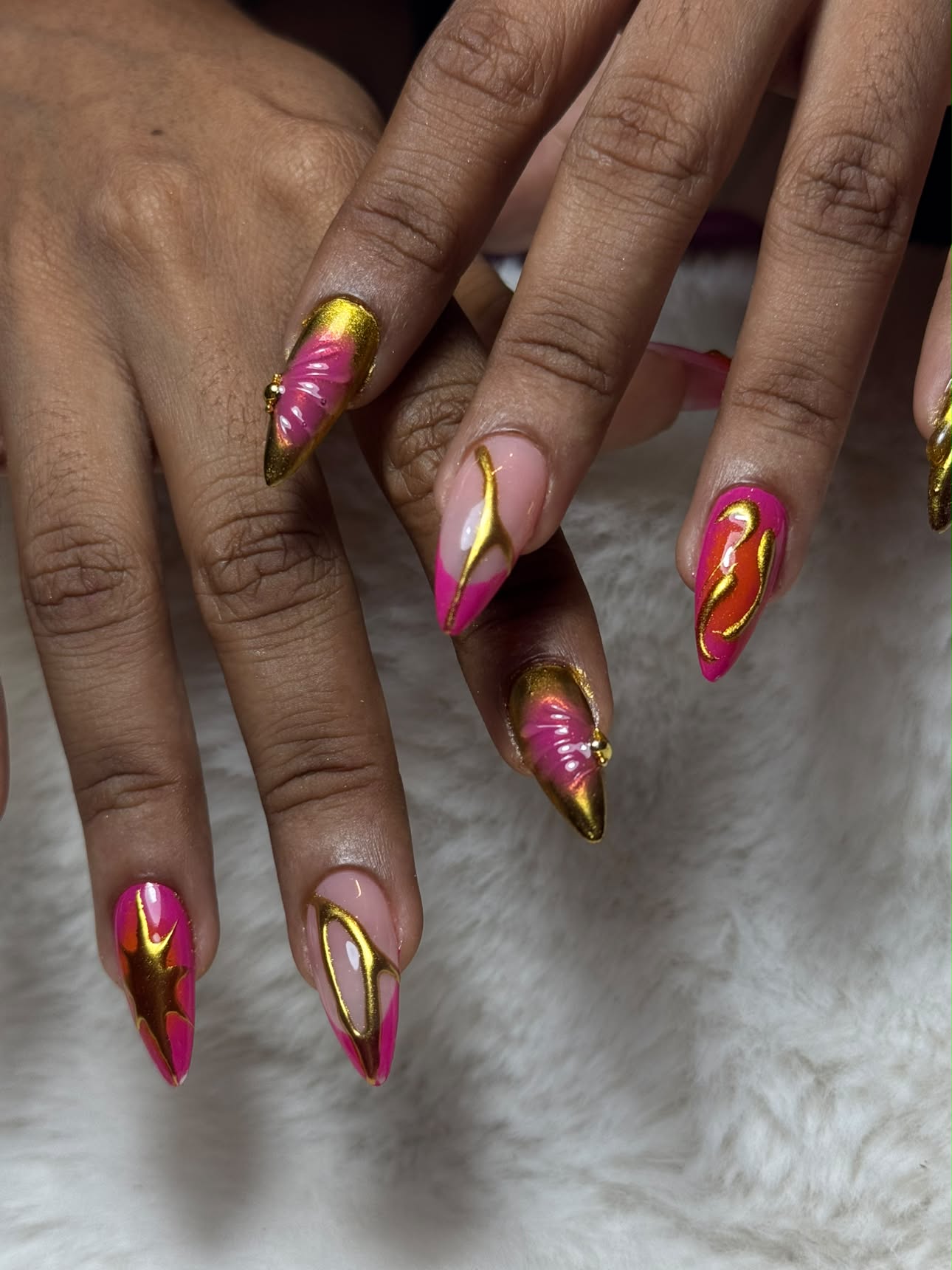 Ongles stiletto roses sculptés de reliefs dorés, posés sur une fourrure claire